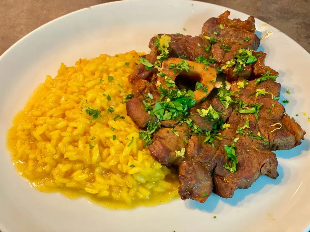 Ossobuco ricetta originale servito con risotto giallo cremoso, guarnito con prezzemolo fresco e scorza di limone.