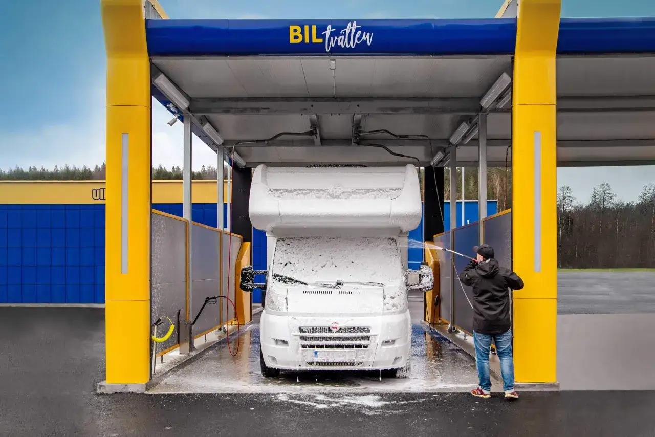 En person tvättar en husbil med skum på en biltvätt. Här får man tvätta bilen hemma, eller åtminstone på en station som denna.