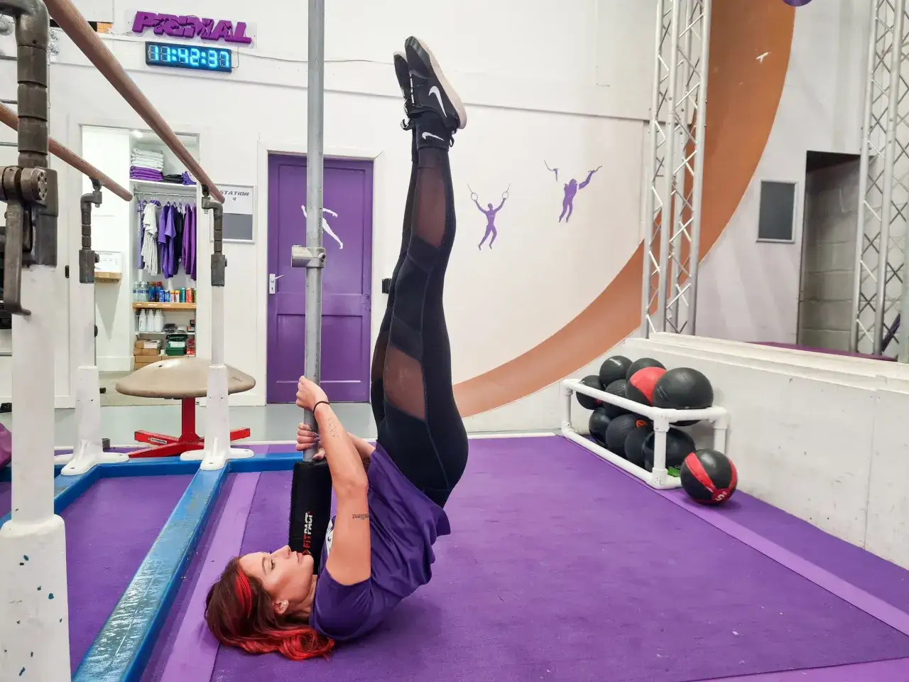 Frau trainiert im Fitnessstudio, um Muskelaufbau zu f&ouml;rdern. Sie h&auml;lt sich an einer Stange fest und hebt ihre Beine.