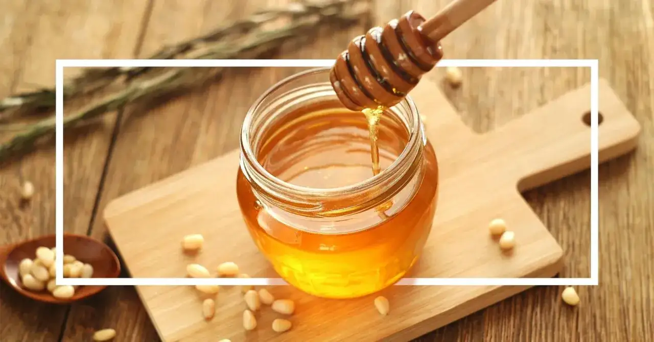 Goldener Honig tropft aus einem Holzst&auml;bchen in ein Glas. Perfekt, um Saunahonig selber zu machen und die Haut zu pflegen.