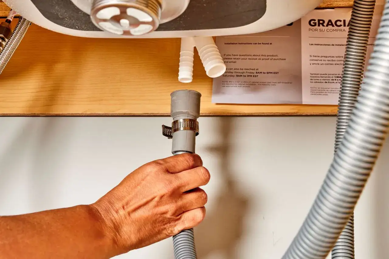 Hand connecting a dishwasher drain hose to a sink drain pipe during installation.