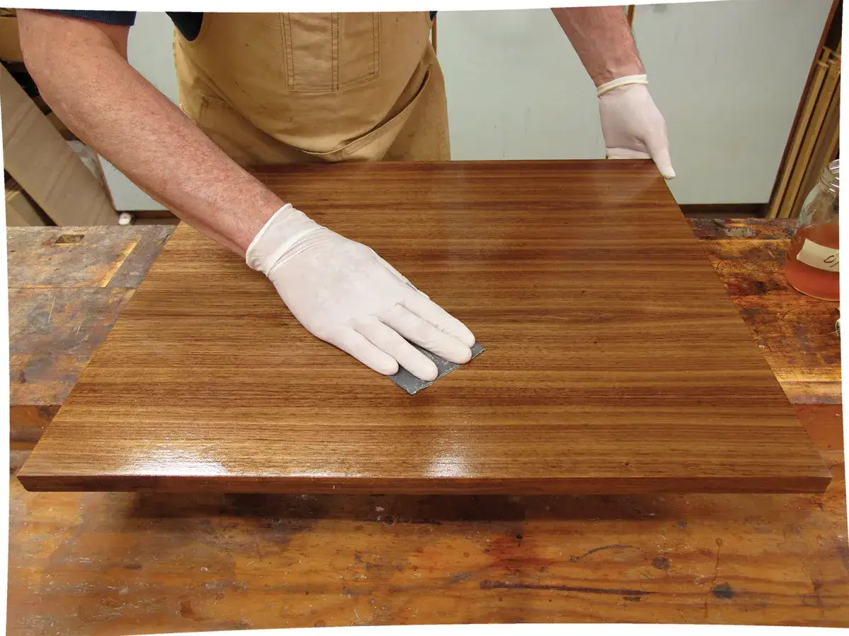 Mano guantata carteggia una superficie di legno lucida, un gesto che ne definisce il significato di finitura e cura.