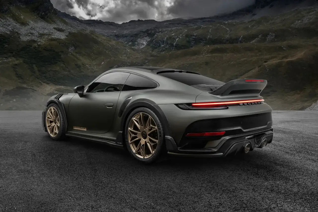 Ein mattschwarzer Techart GTstreet RS mit goldenen Felgen steht auf asphaltierter Stra&szlig;e vor einer Bergkulisse.