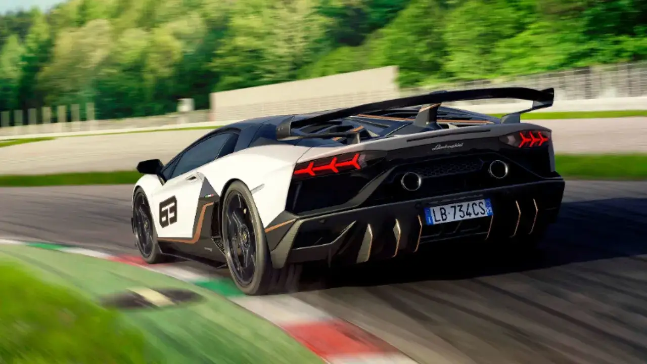 Białe Lamborghini SVJ z czarnym dachem i złotymi akcentami pędzi po torze wyścigowym, zostawiając za sobą smugę kurzu.