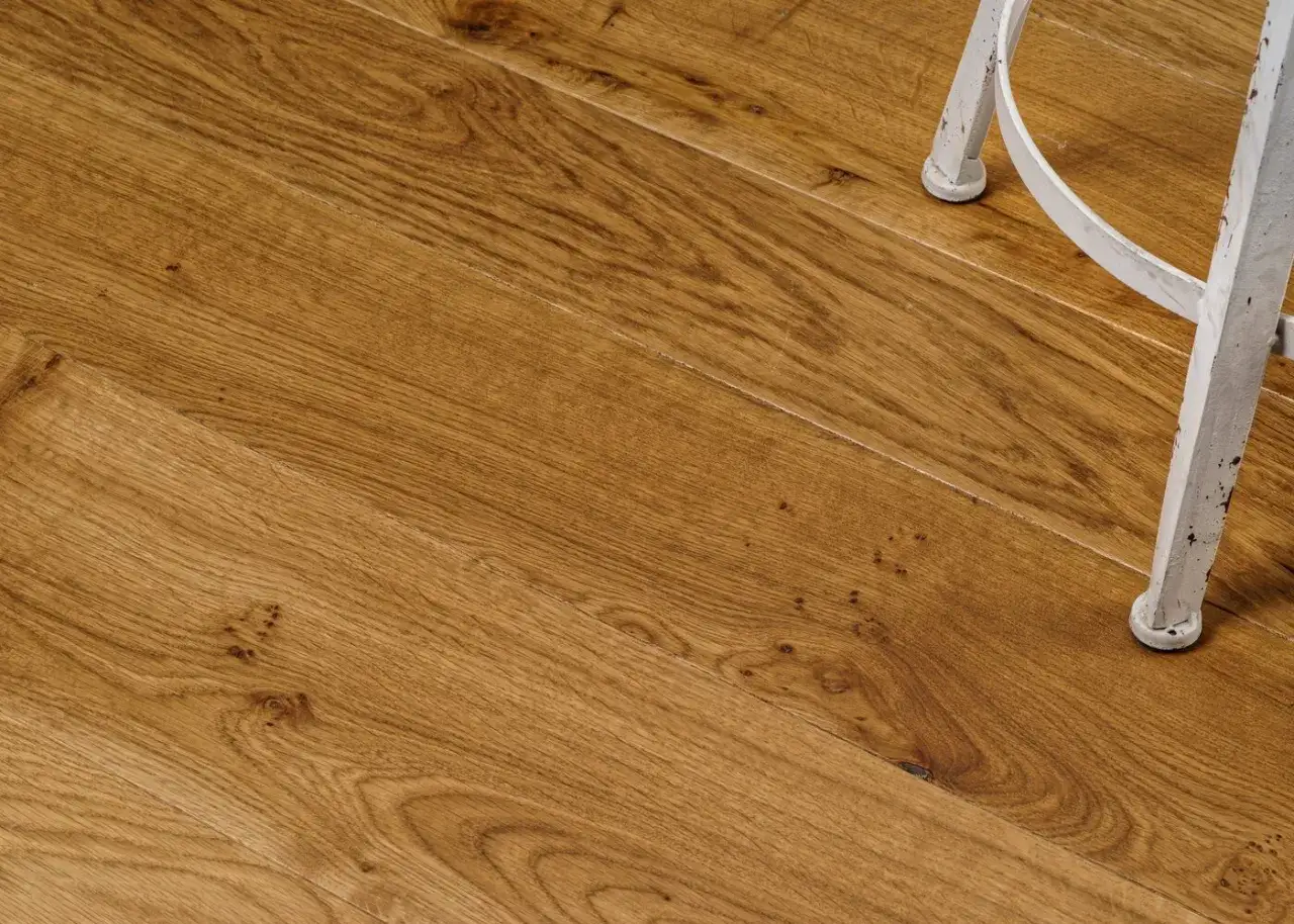 Gros plan sur un parquet huilé ou ciré aux teintes chaudes, avec le pied d'une chaise blanche en arrière-plan.
