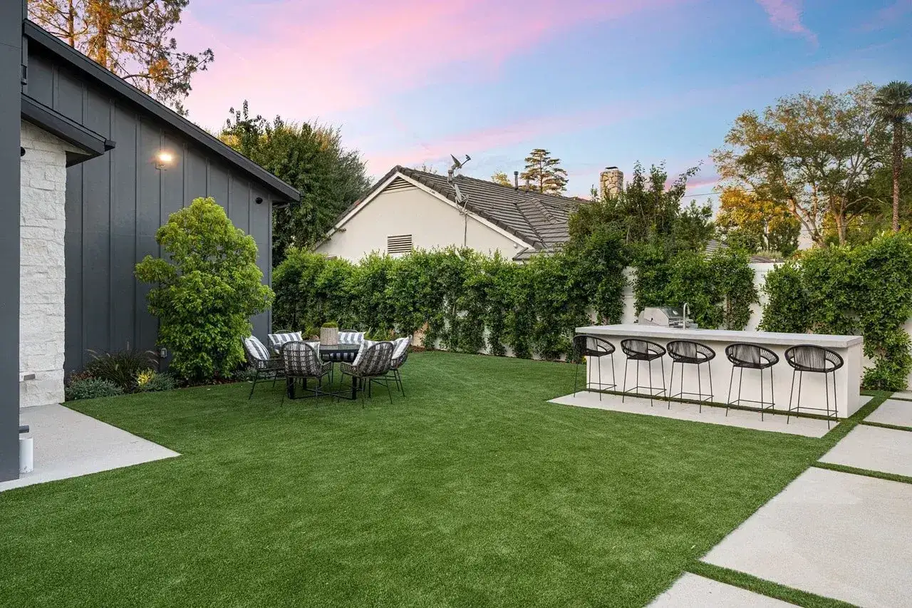 A backyard with artificial grass, outdoor kitchen, and dining set. This image shows how to install artificial grass for a low-maintenance lawn.