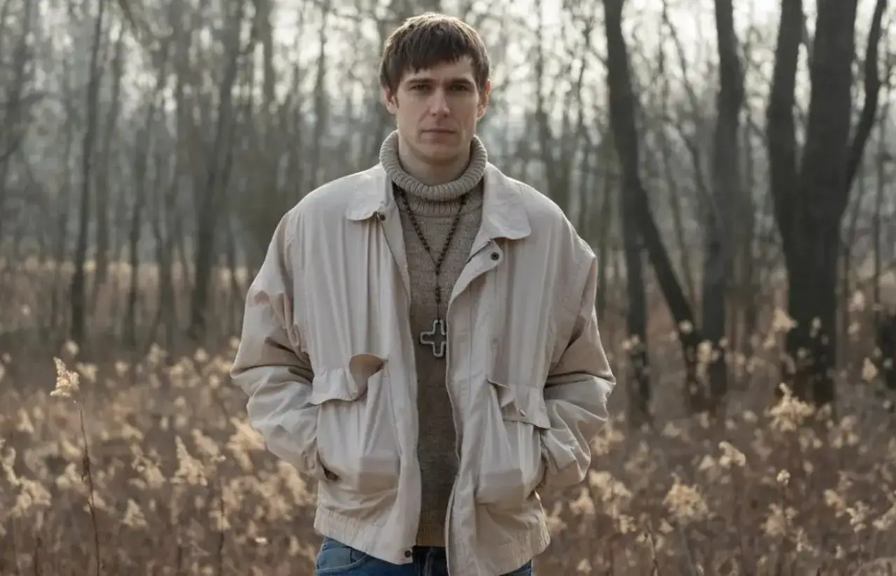 Sebastian Keller w beżowej kurtce i z krzyżem na szyi, jakby szukał swojej żony w zaroślach.