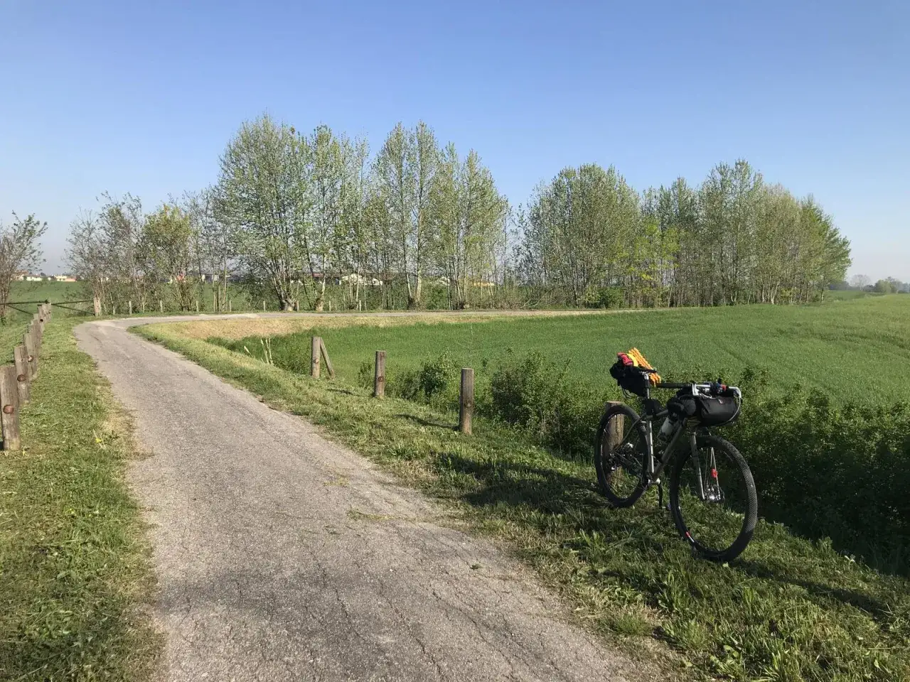 Bicicletta da cicloturismo pronta per un'avventura tra Ferrara e Mantova, su una strada sterrata che attraversa campi verdi sotto un cielo azzurro.