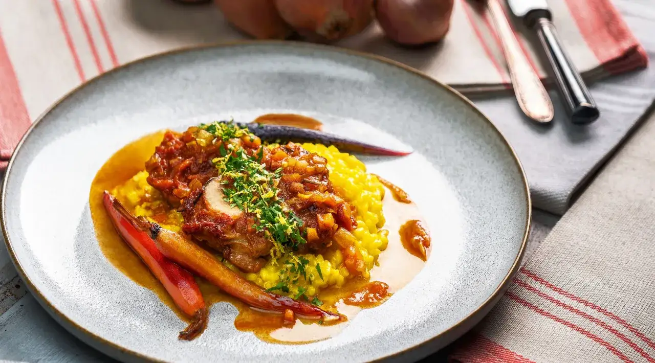 Ein Teller mit Ossobuco, serviert auf Safranrisotto, garniert mit Kr&auml;utern und Karotten. Ein authentisches ossobuco rezept original italienisch.