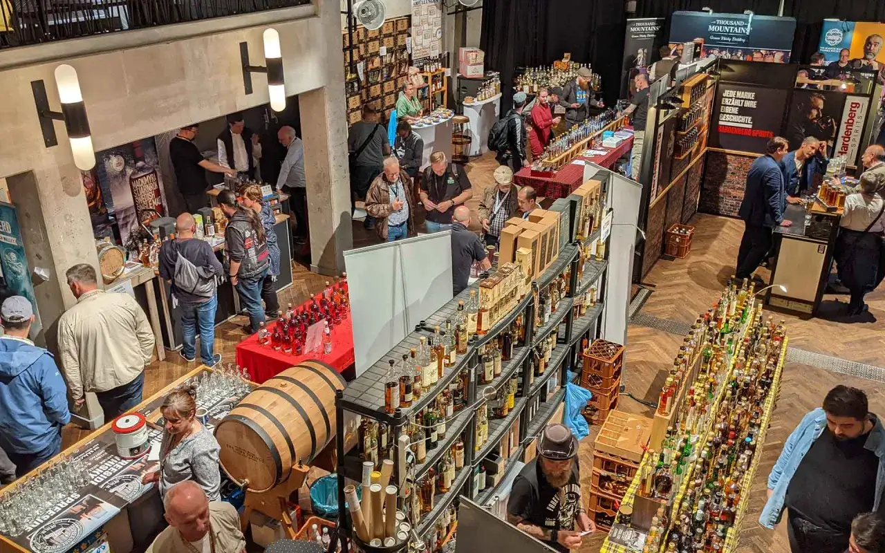Besucher probieren Spree-side Whisky auf einer Messe. Viele Flaschen und ein Fass sind ausgestellt.