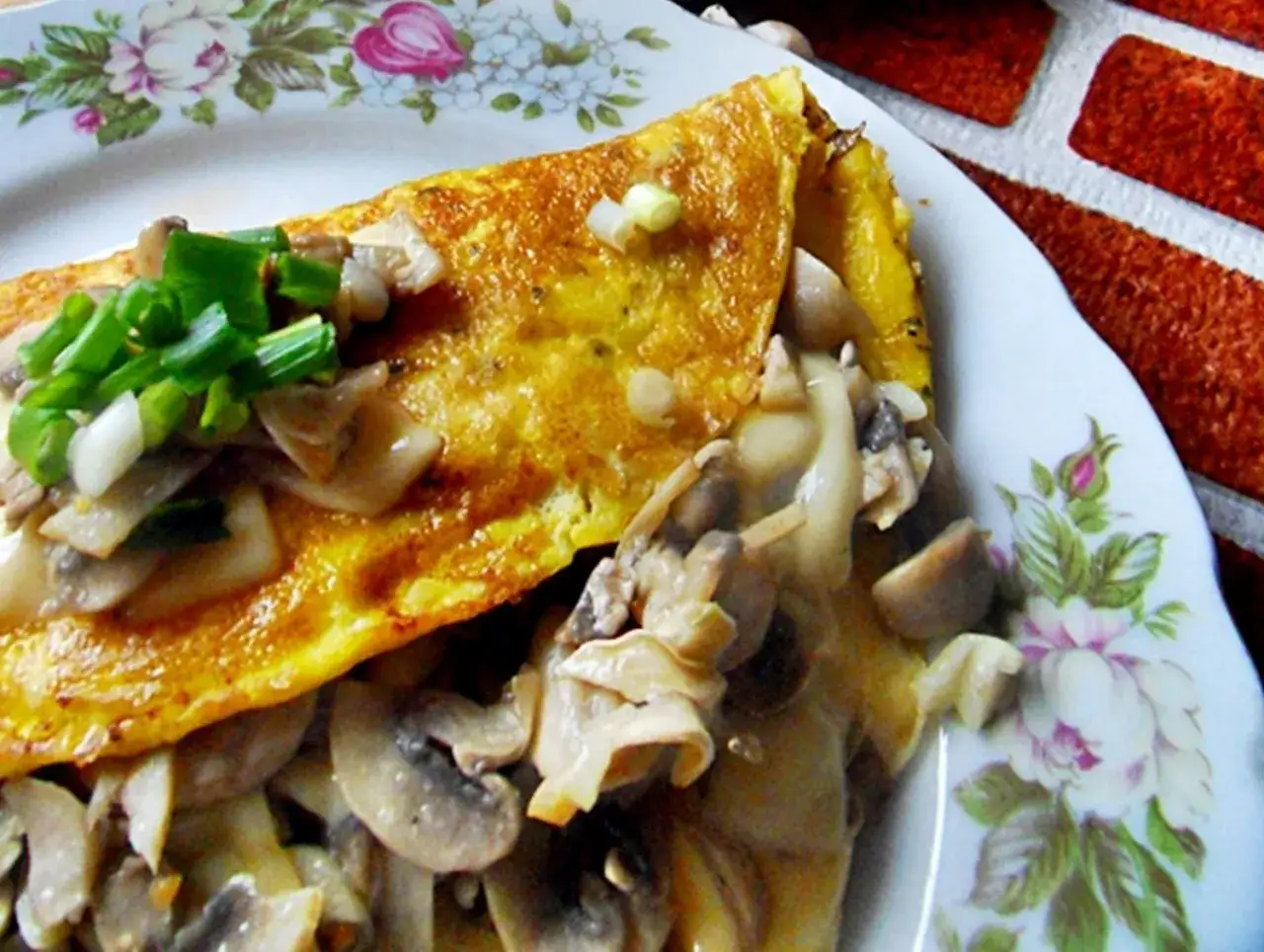 Złocisty omlet z pieczarkami i szczypiorkiem, podany na talerzu z kwiatowym wzorem. Pyszne śniadanie gotowe!