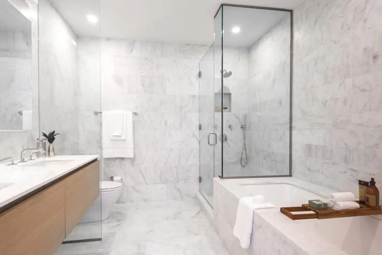Elegante progetto bagno con vasca e doccia separate, rivestimenti in marmo bianco e mobile lavabo in legno.