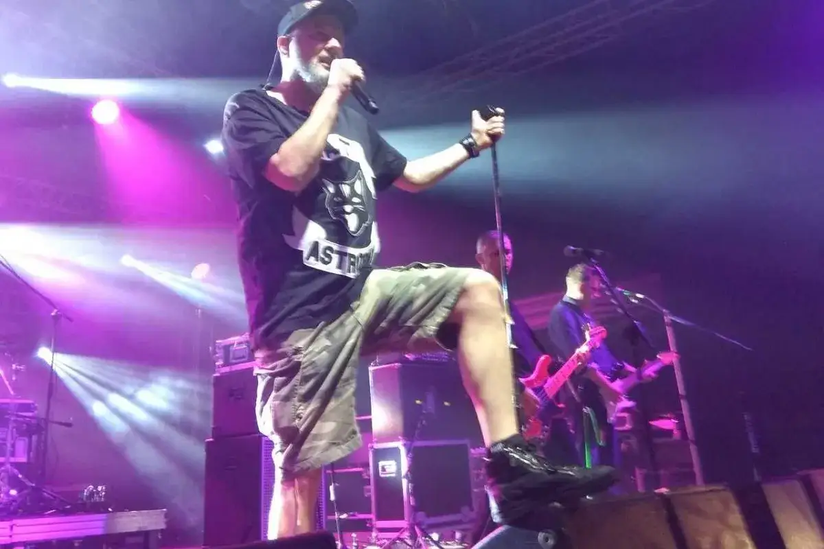 Strachy na lachy wokalista z mikrofonem na scenie, w tle zespół i fioletowe światła.