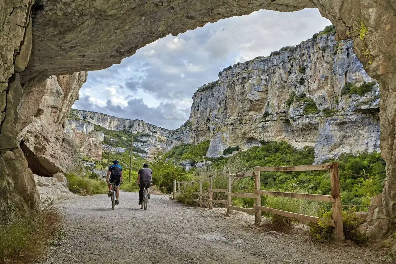 Dos ciclistas exploran la **Foz de Lumbier ruta**, un impresionante cañón con paredes rocosas y vegetación exuberante.