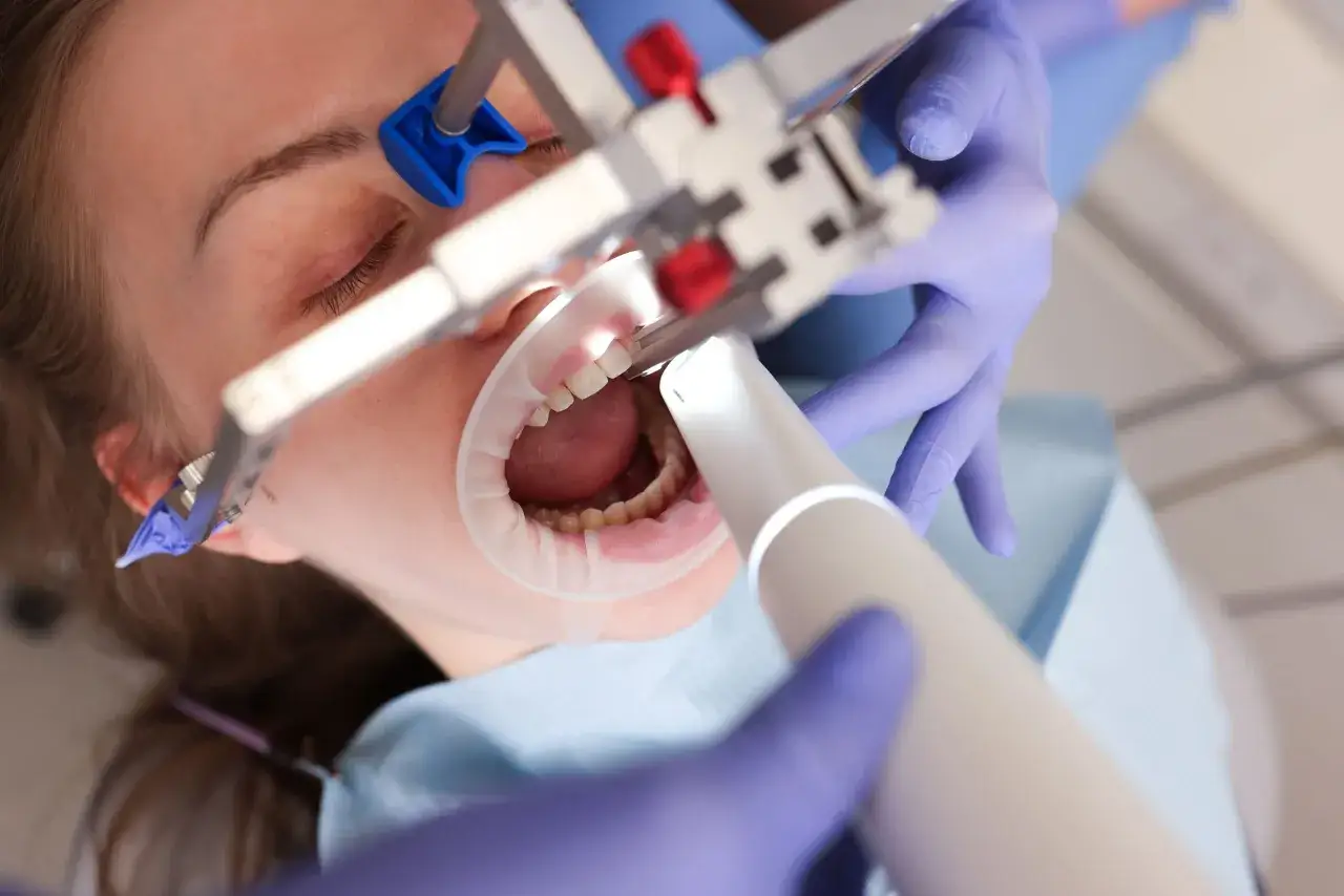 Dentysta wykonuje szynowanie zębów w leczeniu paradontozy. Pacjentka ma otwarte usta z retraktorem.