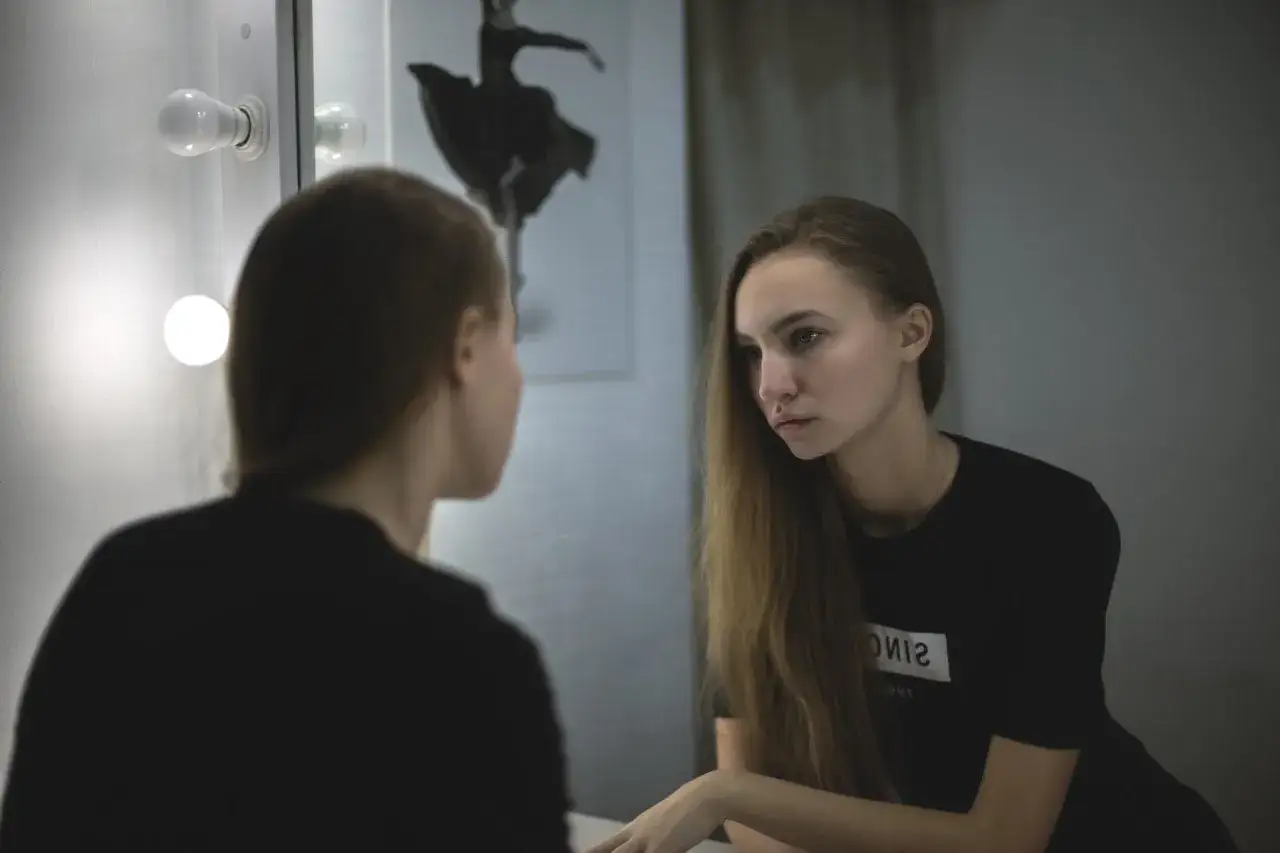 Una ragazza si guarda allo specchio, riflettendo. Le cose non cambiano, siamo noi che cambiamo, come la ballerina sullo sfondo.