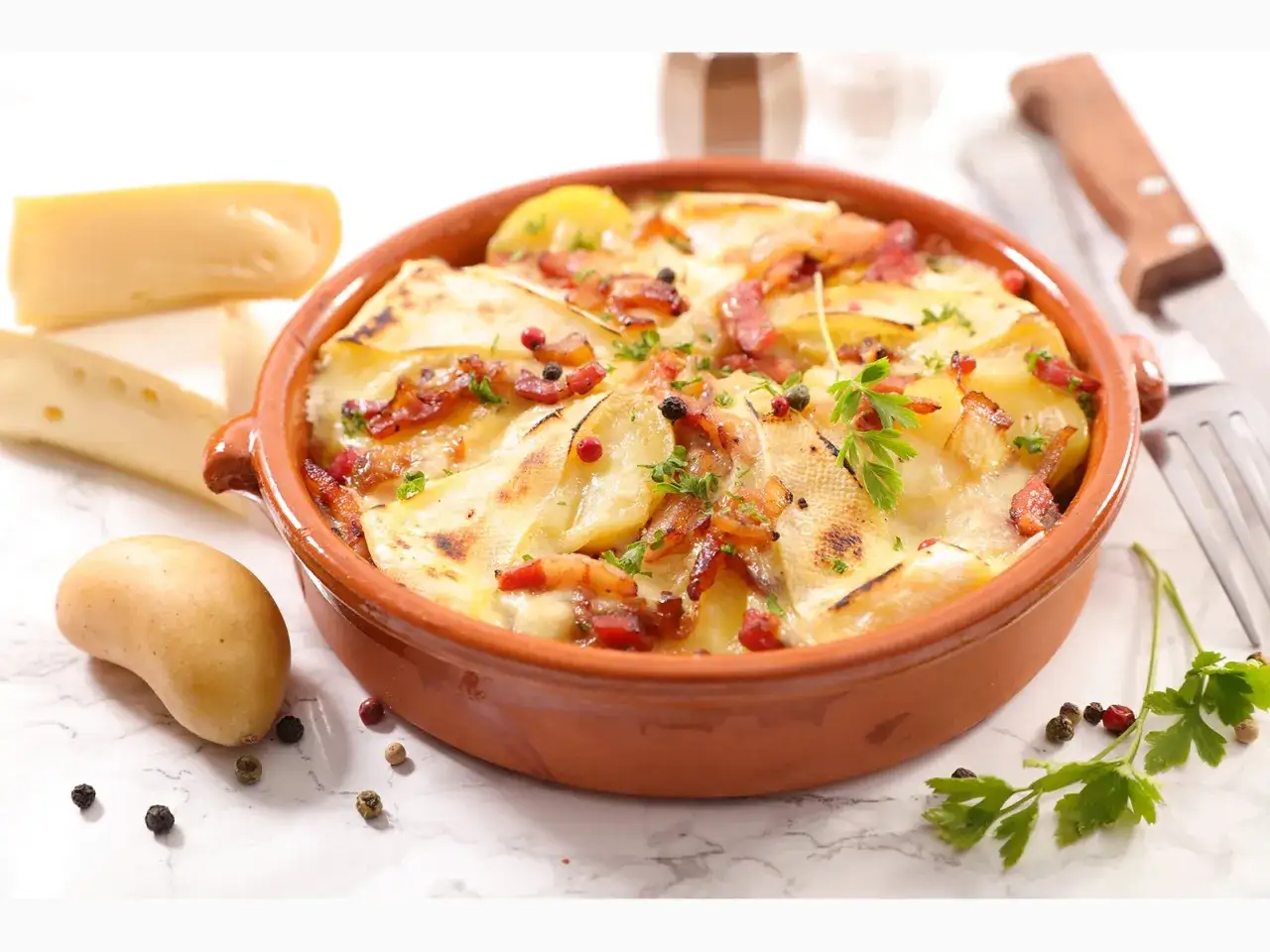 Herzhaftes Tartiflette-Rezept: Kartoffeln, Speck und K&auml;se in einer Auflaufform, garniert mit Petersilie und Pfefferk&ouml;rnern.