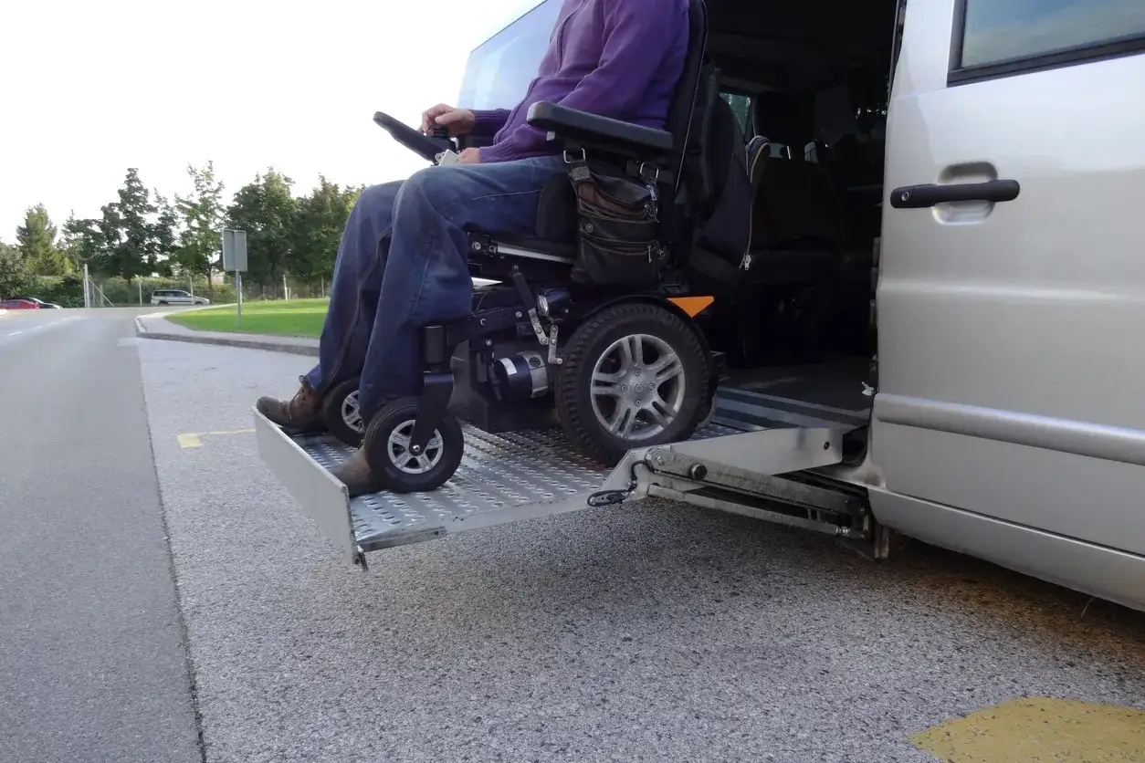 Persona su sedia a rotelle elettrica su una pedana estesa, pronta per essere caricata in macchina.
