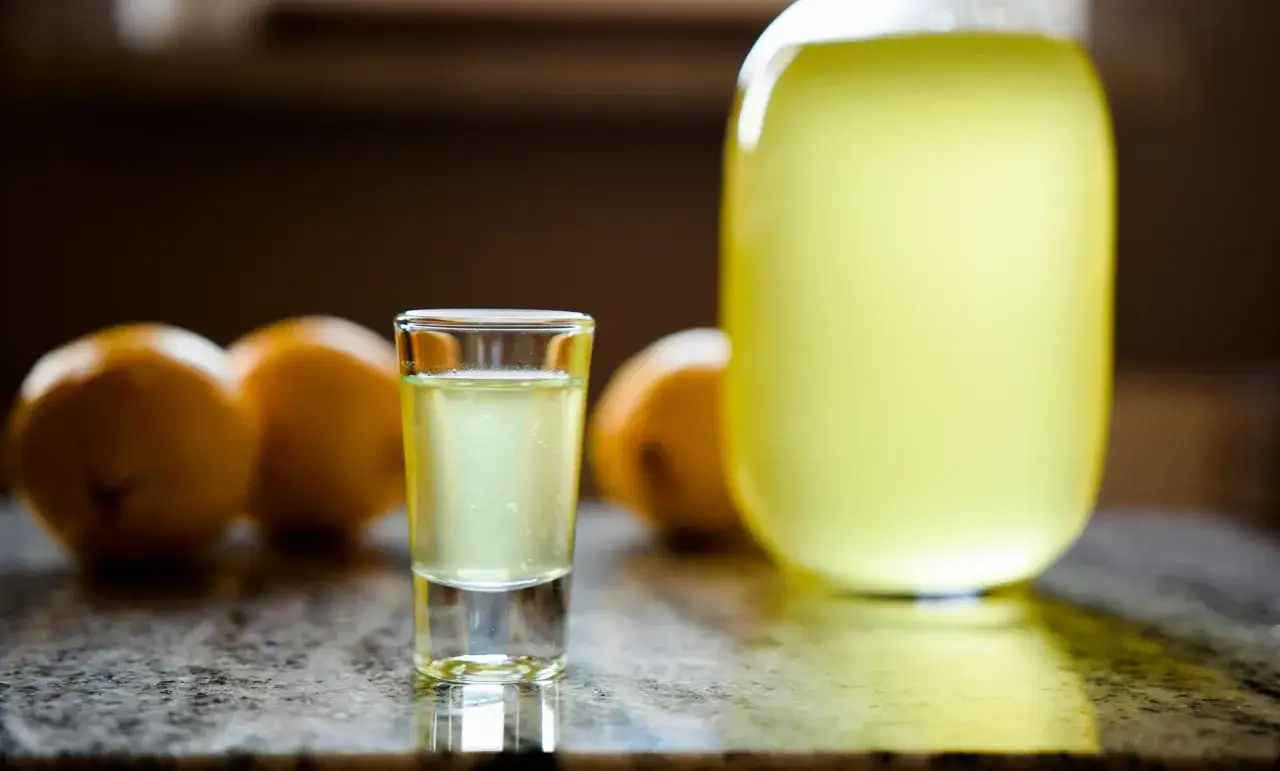 Szklaneczka orzeźwiającego likieru cytrynowego limoncello obok cytryn i dużej butelki tego włoskiego specjału.