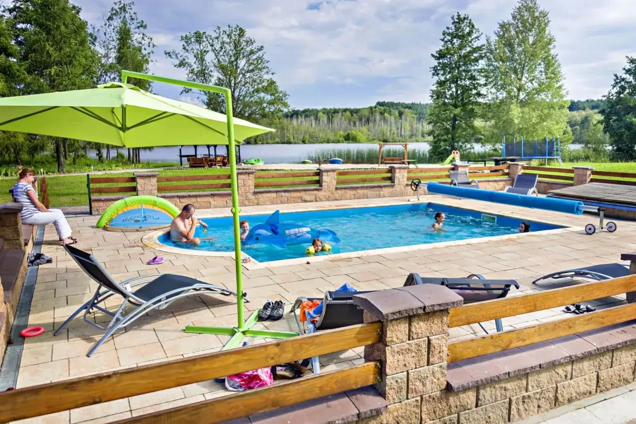 Rodzinna rekreacja w hotelu nad jeziorem Wielkopolska. Dzieci bawią się w basenie, rodzice odpoczywają na leżakach.