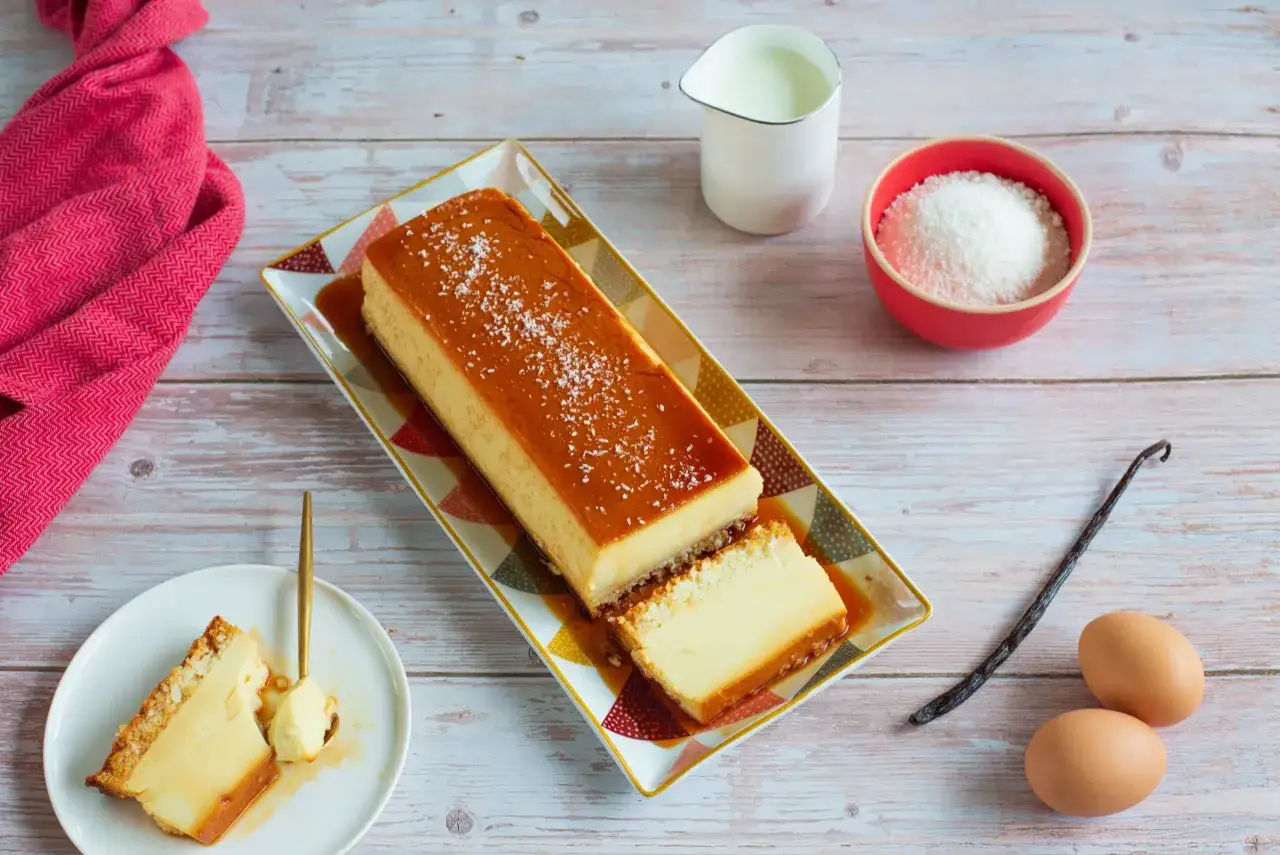 Un d&eacute;licieux flan coco, saupoudr&eacute; de noix de coco r&acirc;p&eacute;e, est pr&ecirc;t &agrave; &ecirc;tre d&eacute;gust&eacute;. Des ingr&eacute;dients frais comme des &oelig;ufs et une gousse de vanille sont &agrave; proximit&eacute;.