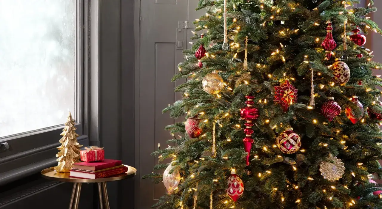 Comment faire un beau sapin : un arbre de Noël décoré de boules rouges et dorées, de guirlandes lumineuses et d'ornements scintillants. À côté, une petite table avec un sapin doré et des cadeaux.