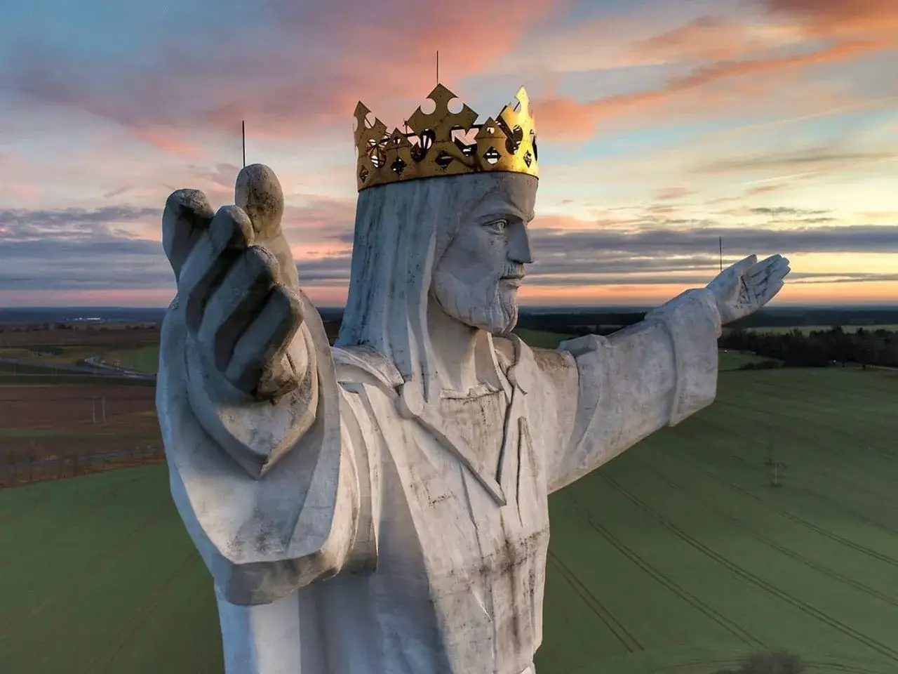 Największy pomnik Jezusa na świecie, z koroną na głowie, wznosi się nad polami o zachodzie słońca.