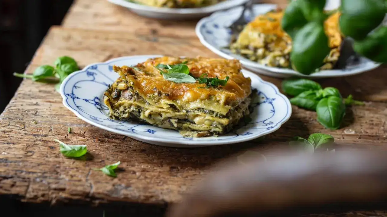 Herzhafte Spinat-Lasagne mit goldbrauner Käsekruste, garniert mit frischem Basilikum, serviert auf einem rustikalen Holztisch.