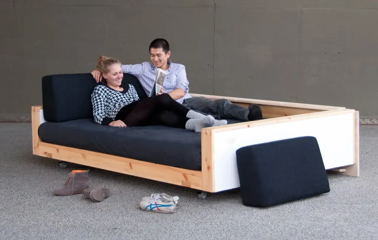 Ein Paar entspannt auf einem selbstgebauten Sofabett. Die Holzkonstruktion und die dunklen Polster laden zum Verweilen ein.
