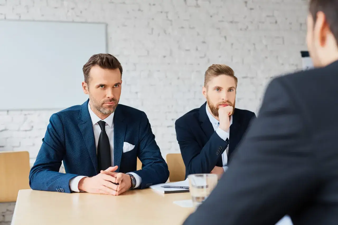 Dwóch mężczyzn w garniturach siedzi przy stole, omawiając umowę B2B.