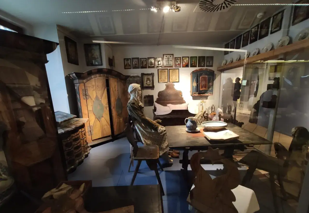 Wrocław Muzeum Etnograficzne: ekspozycja dawnej izby z manekinem w stroju ludowym, zdobionymi meblami i obrazami na ścianach.