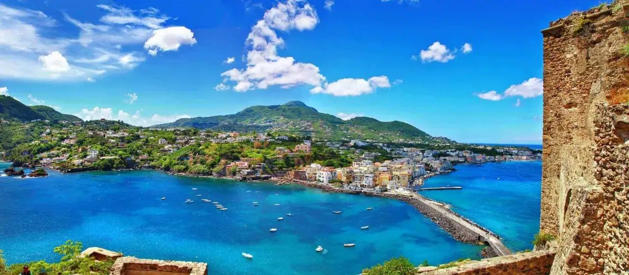 Vista panoramica dell'isola d'Ischia con il mare blu intenso, case colorate e montagne verdi.