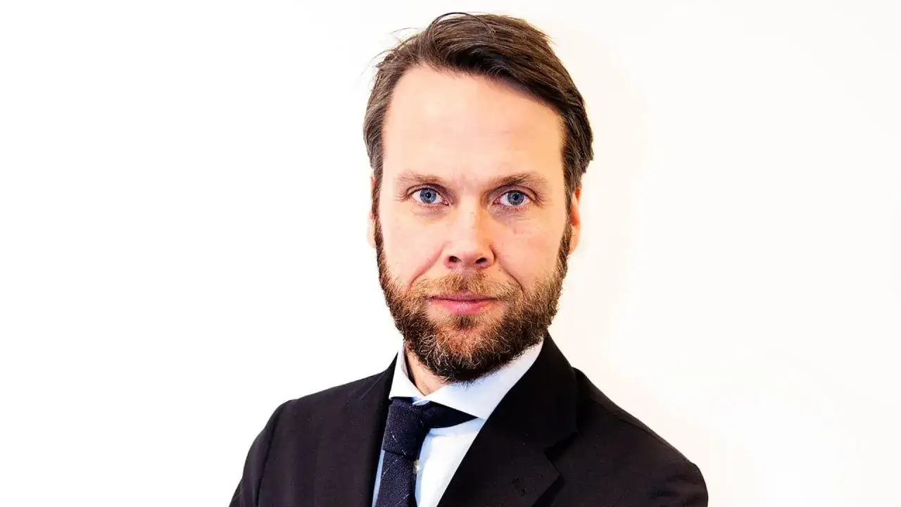 Porträtt av Magnus Alselind, en man med skägg och blå ögon, klädd i kostym och slips.