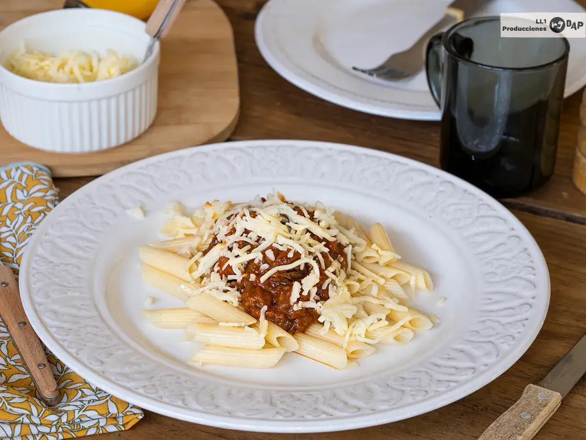 Macarrones con carne picada, cubiertos de queso rallado, servidos en un plato blanco con un diseño floral.