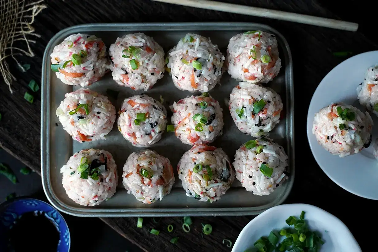 Urocze kulki sushi z ryżu, łososia i szczypiorku, ułożone na metalowej tacy, gotowe do podania.