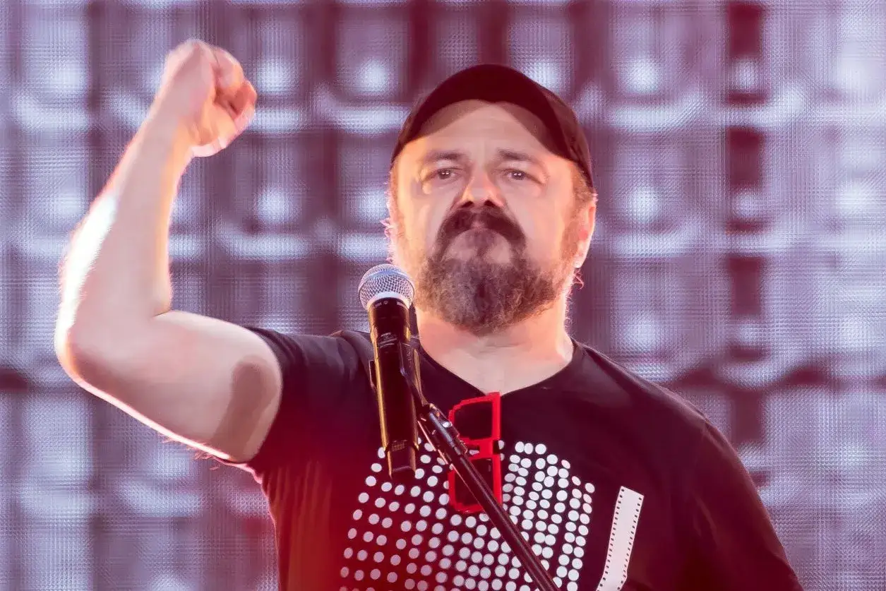 Dr Misio znikam! Wokalista z podniesioną pięścią przed mikrofonem, w czapce i z brodą.