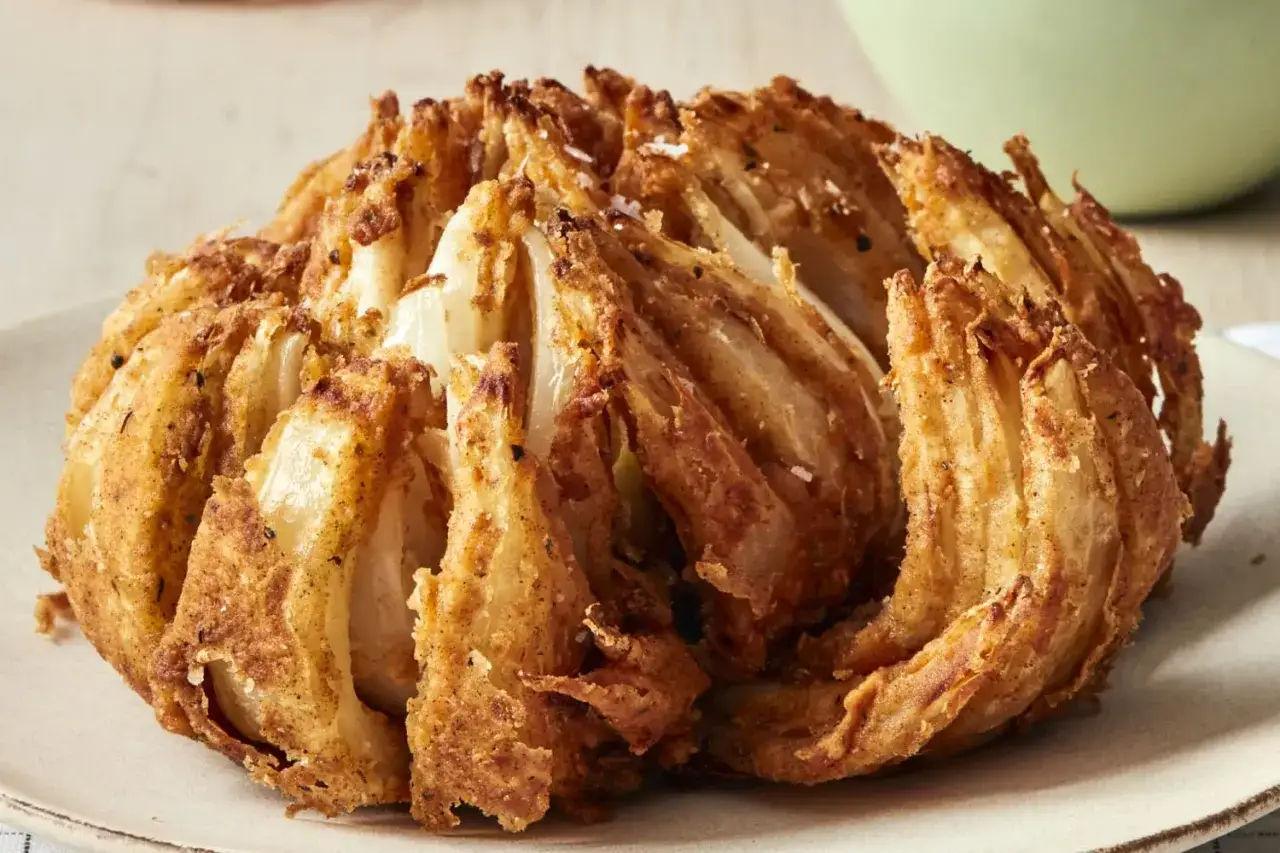 Knusprig frittierte Blooming Onion, goldbraun und mit Gewürzen bestreut, auf einem Teller.