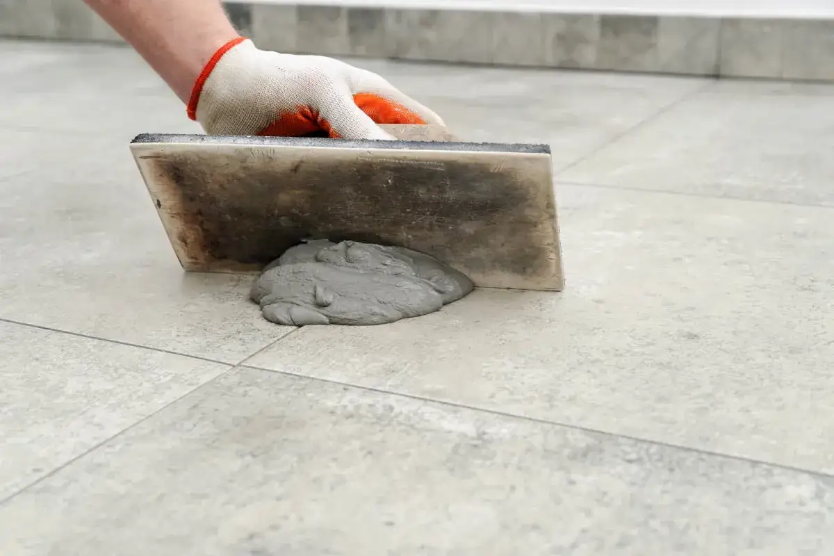 Mano guantata stende stucco grigio con spatola per stuccare piastrelle.
