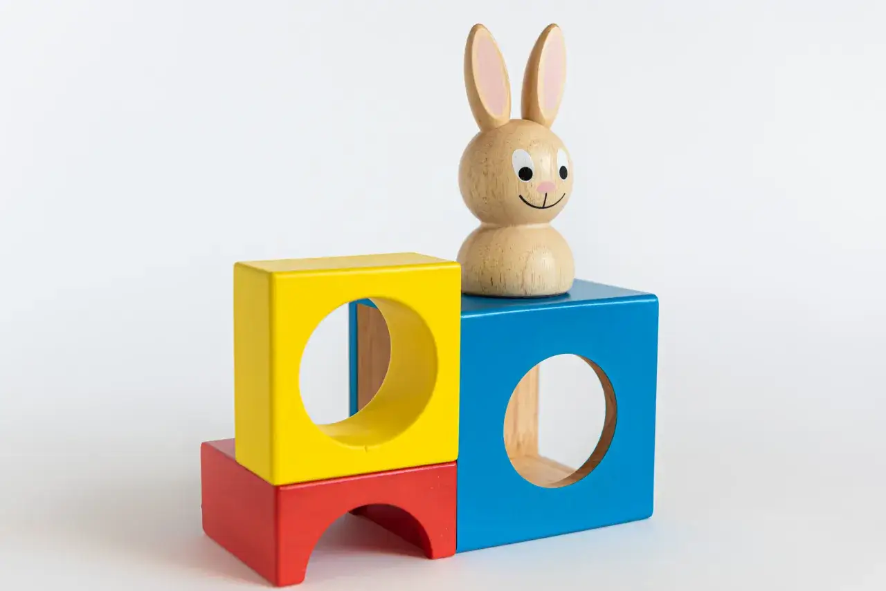 Drewniany króliczek na niebieskim klocku, obok żółtego i czerwonego. Czy króliki są inteligentne? Ten wygląda na zamyślonego.