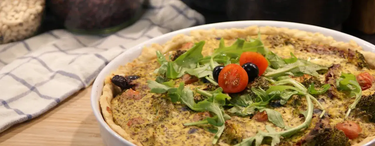 En gyllene vegansk paj med broccoli, tomater och oliver, toppad med f&auml;rsk ruccola.
