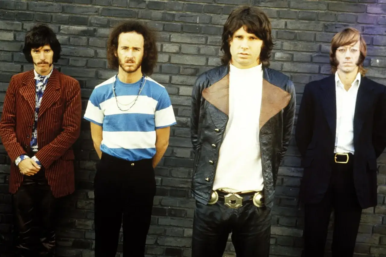 Członkowie The Doors stoją przed ceglaną ścianą. Od lewej: Robby Krieger, John Densmore, Jim Morrison, Ray Manzarek.