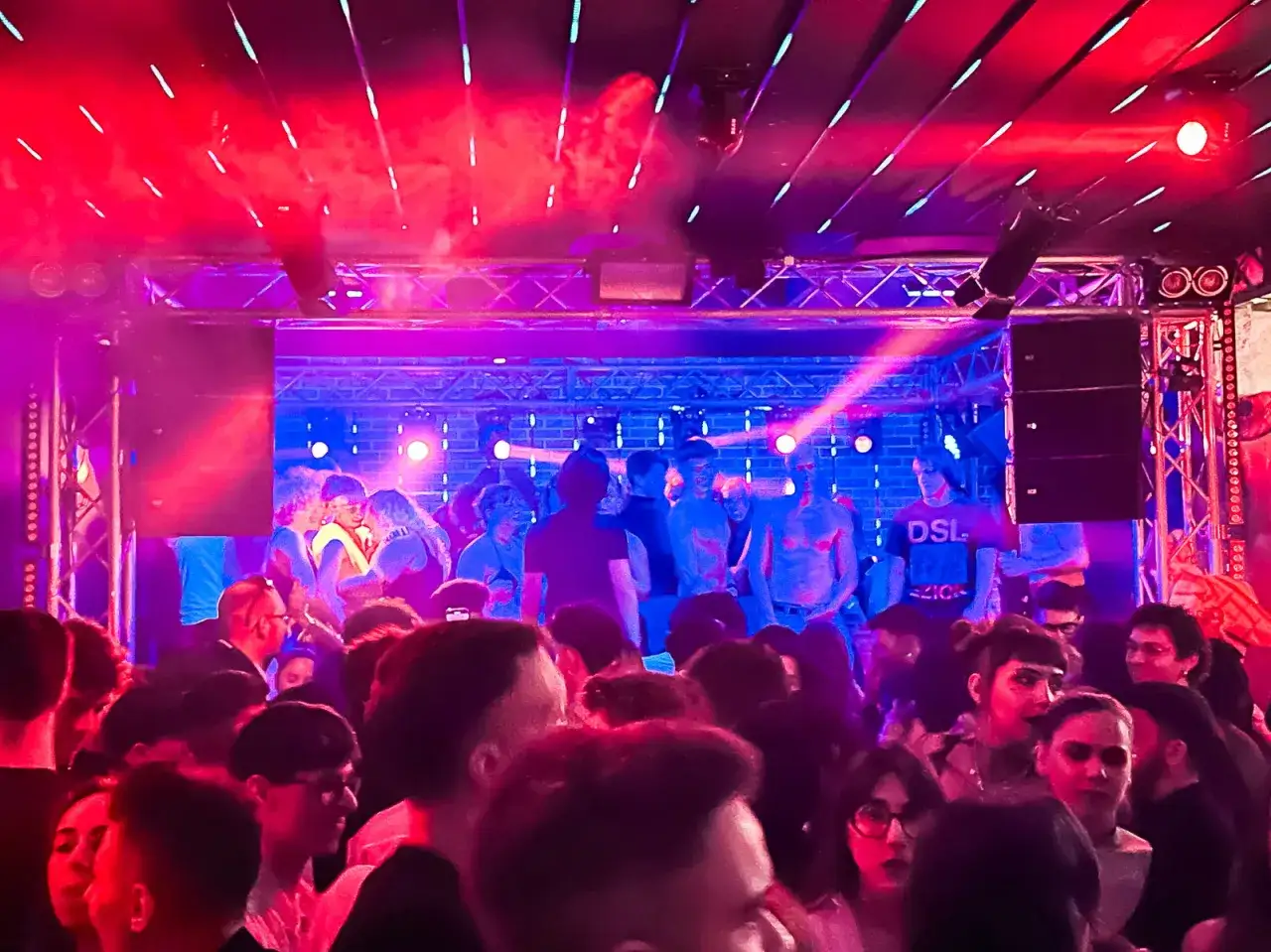 A vibrant gay Venice party scene, with people dancing under colorful lights.
