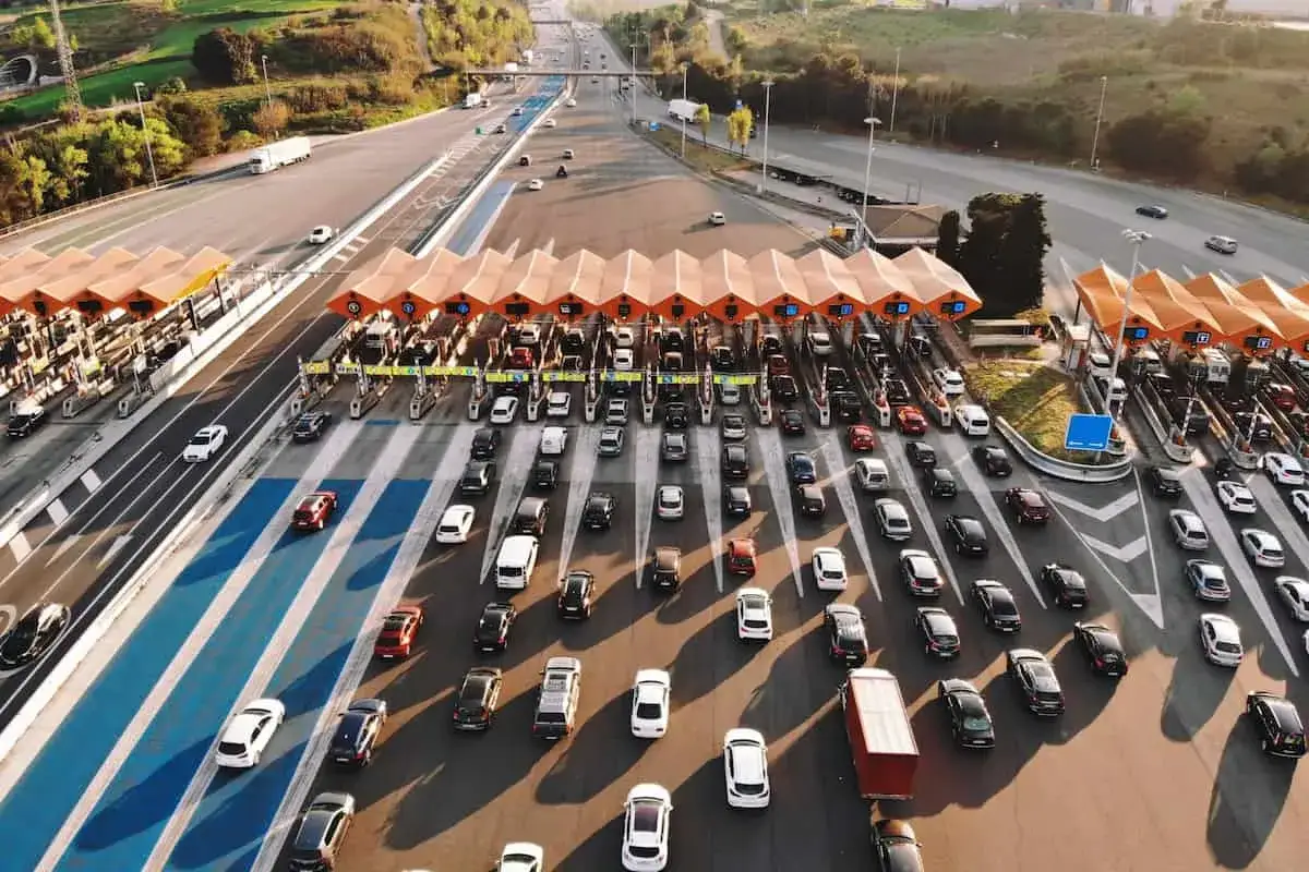 Vista aérea de un gran atasco de coches en una autopista con peajes. Los vehículos esperan en varias filas para pasar.