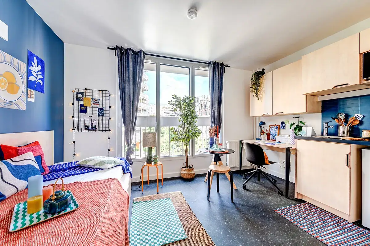 Habitación moderna con cama, escritorio y cocina. Un gran arco de luz ilumina el espacio, creando un ambiente acogedor.