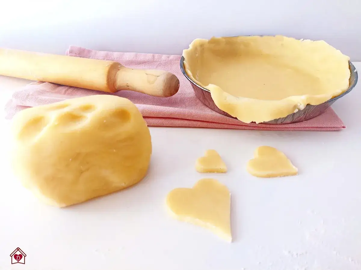 Impasto per crostata senza glutine pronto per essere lavorato, con cuoricini ritagliati e base già preparata in teglia.