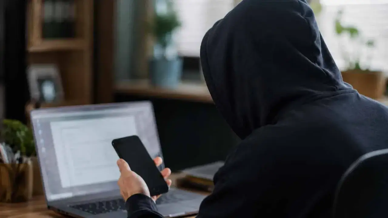 Osoba w kapturze korzysta z laptopa i telefonu. Grozi jej kara za kradzież powyżej 1000 zł.