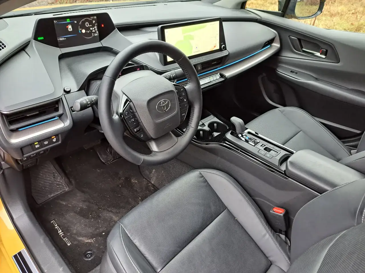 Wnętrze Toyoty Prius. Widoczne fotele, kierownica, deska rozdzielcza z ekranem nawigacji. Ile miejsc? Zazwyczaj 5.