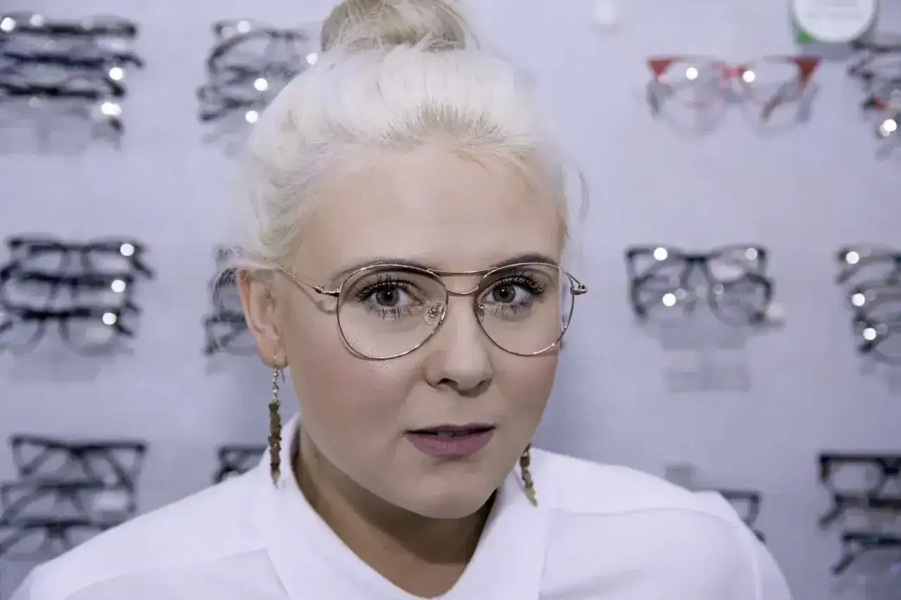 Kobieta z blond włosami w okularach z różowymi oprawkami, wybiera nowe okulary w salonie optycznym.