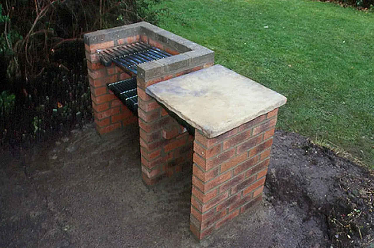 Barbacoa de ladrillo con parrilla y encimera de piedra, lista para hacer barbacoas en el jardín.