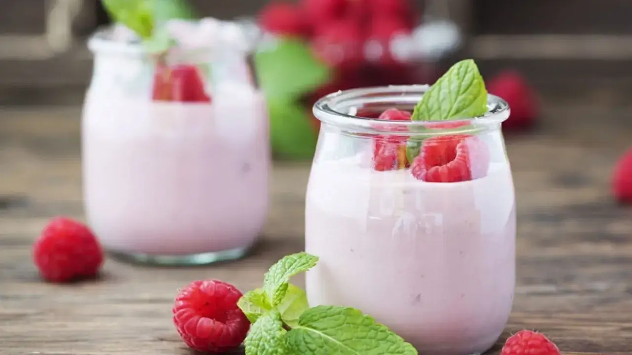 Delicioso helado de yogur casero con frambuesas frescas y hojas de menta, servido en pequeños frascos de vidrio sobre una mesa de madera.